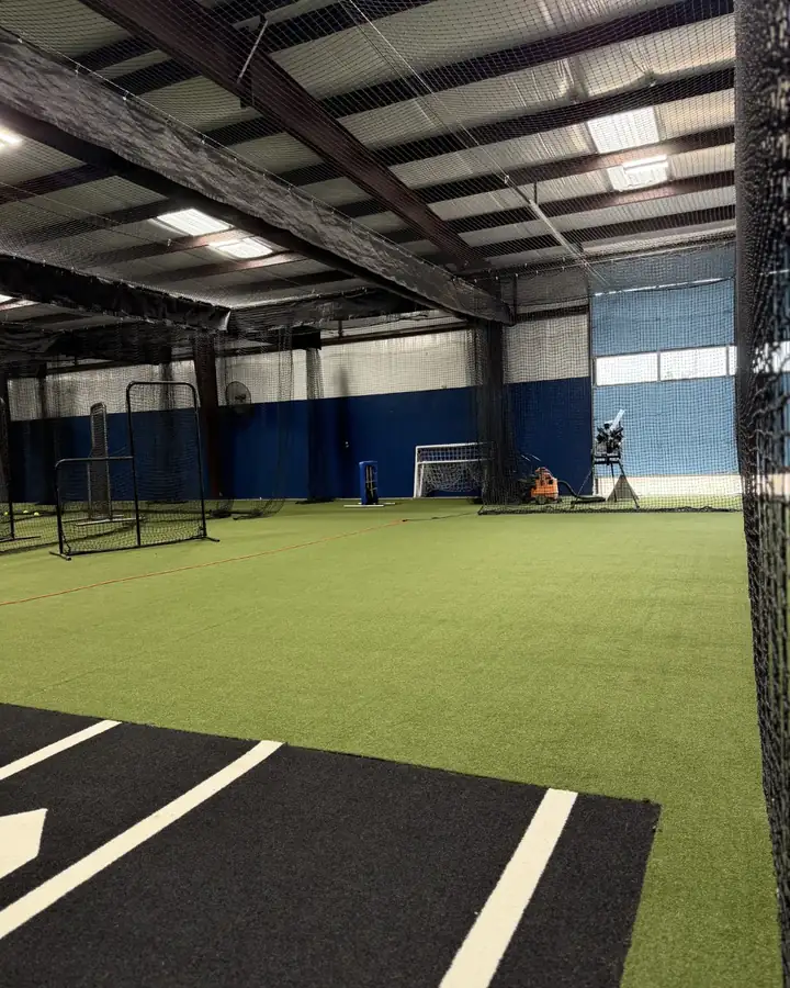 Open turf training area with pitching screens and a pitching machine inside Home Plate Sports